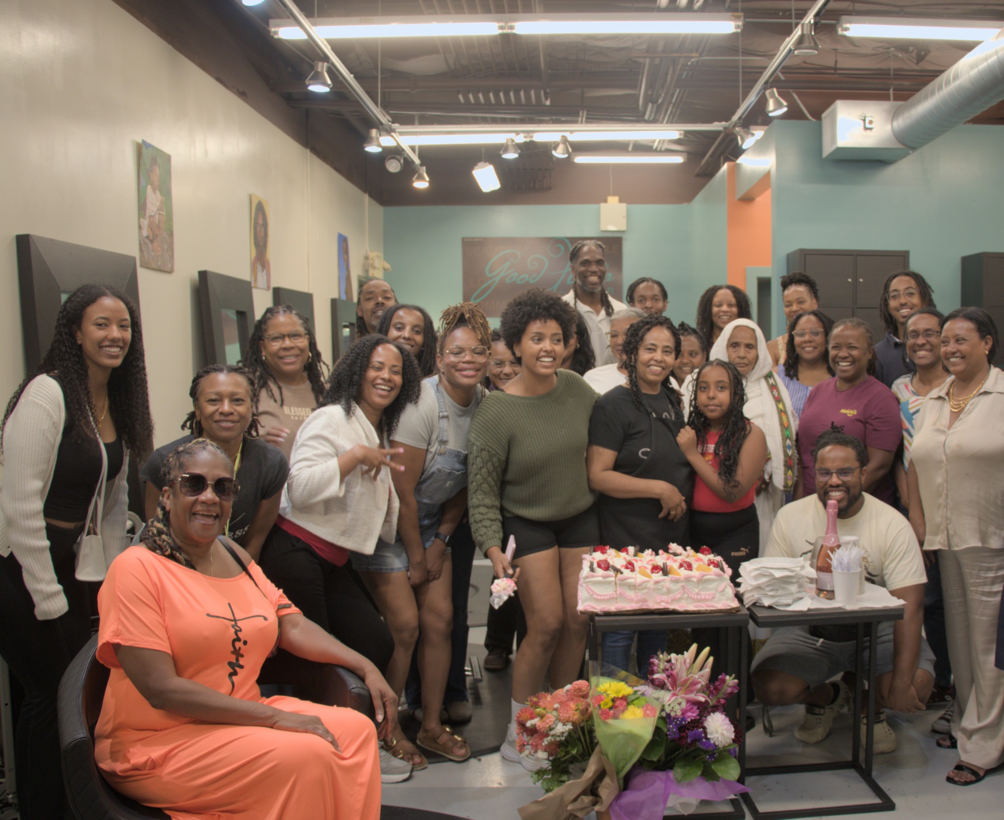Clients, family, and friends celebrating Lemlem’s retirement inside Good Hair Salon. Ela stands near the center in green; Lemlem stands just to her right in black; Esrom is in the back row near the right edge.